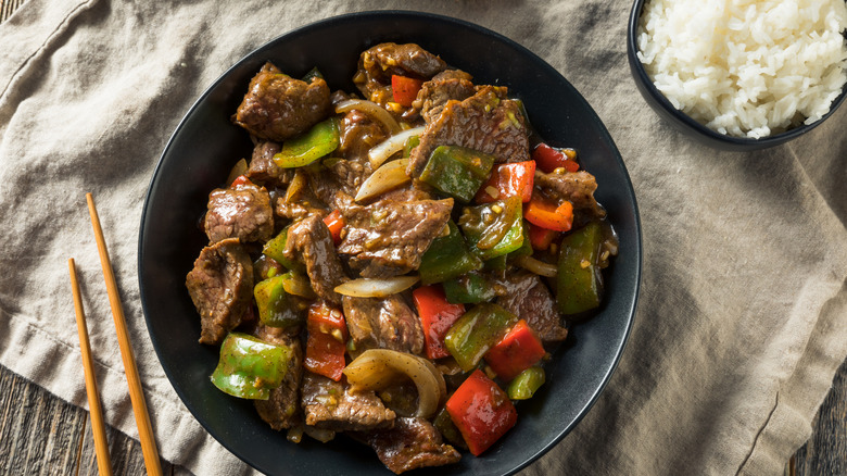 A bowl of Chinese pepper steaks with chopsticks on the side.