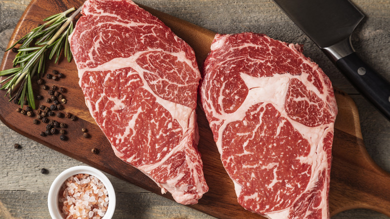 Two steaks on a cutting board next to a sprig of rosemary.
