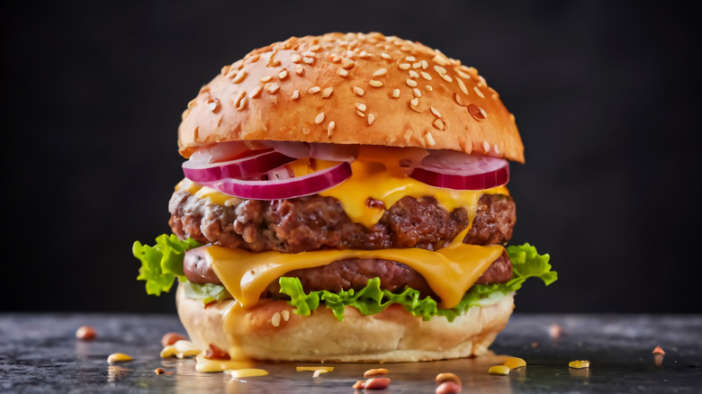 A double cheeseburger with red onion and lettuce against a black background.