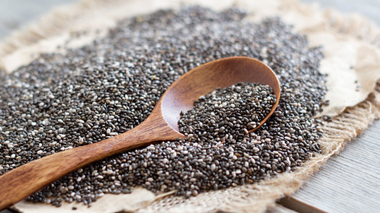 Chia seeds spread out on a table with a wooden spoon in the center.