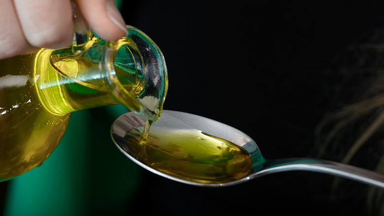 Oil being poured onto a stainless steel spoon.