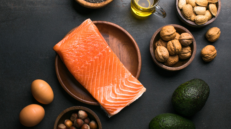 Table with a plate of salmon, a bowl of walnuts, a bowl of chia seeds, and a container of oil.