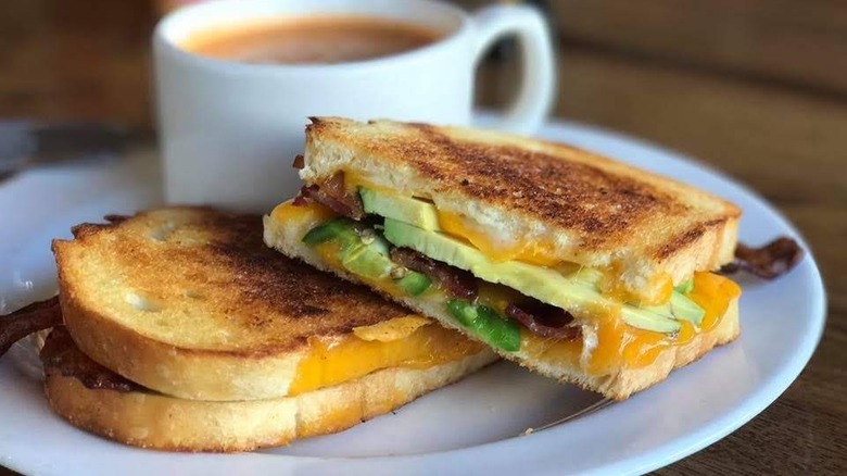 Grilled cheese with avocado on a plate next to a coffee mug