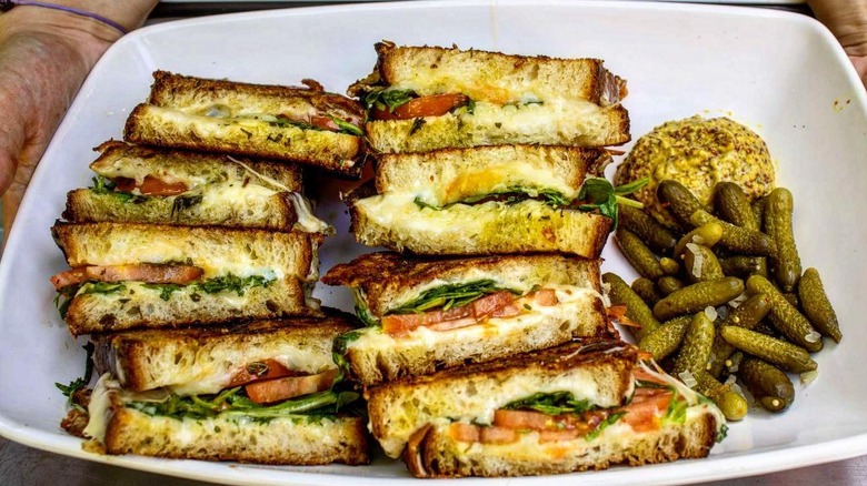 Eight halves of grilled cheese alongside pickles, on a tray