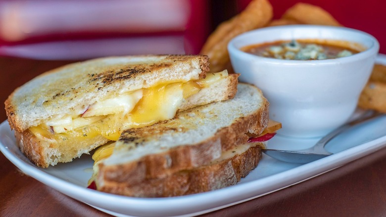 a tray with grilled cheese, a bowl of soup and onion rings.