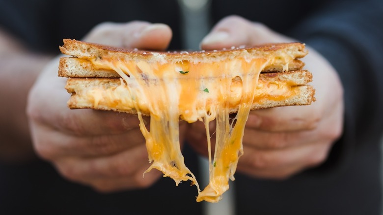 hands holding gooey grilled cheese split in half