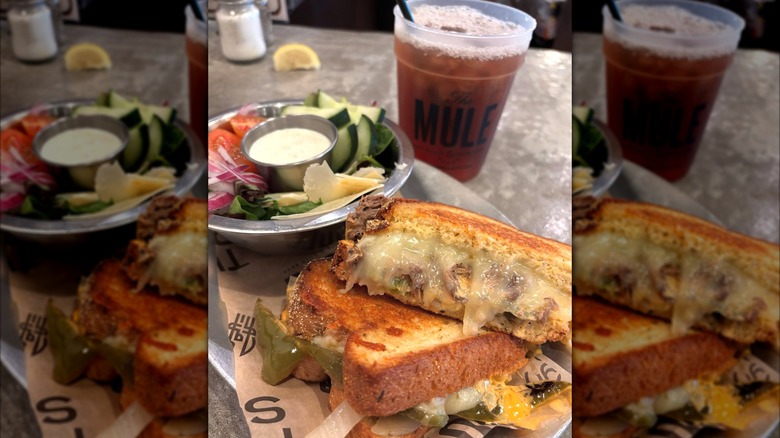 a table with grilled cheese, salad with dip, and a drink on a glass that reads "mule"