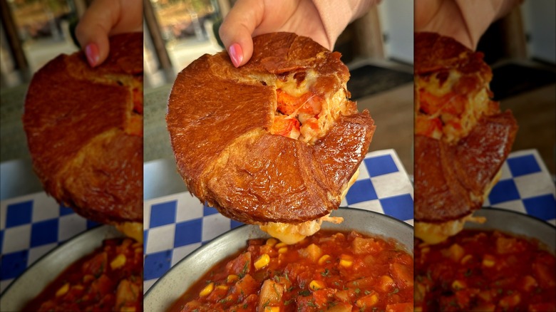 hand holding a croissant lobster grilled cheese on top of a bowl of soup
