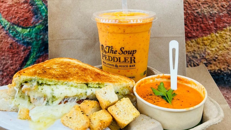 Grilled cheese, croutons, tomato soup and the soup peddler juice on a table