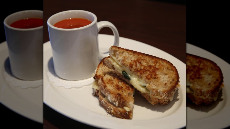 A plate with a mug with soup and grilled cheese