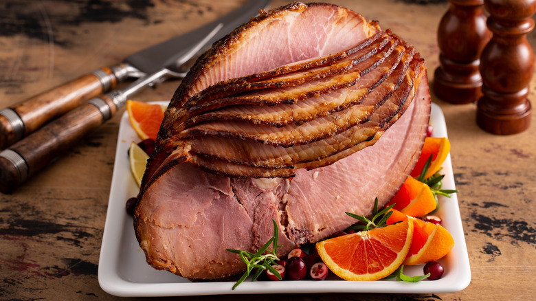 Spiral-sliced ham with oranges on tray on wodden rustic table