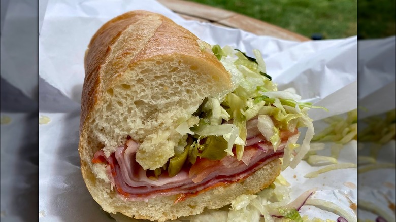 A half Italian sub on a roll filled with layers of deli meats, provolone, shredded lettuce, and sliced onions