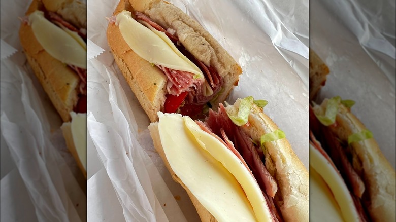 A halved Italian sub on a roll with slices of salami, ham, and provolone, layered with tomatoes and shredded lettuce