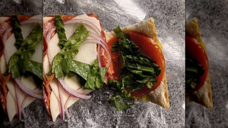 An open Italian sub with layers of pepperoni, provolone, sliced red onion, tomato, and chopped lettuce