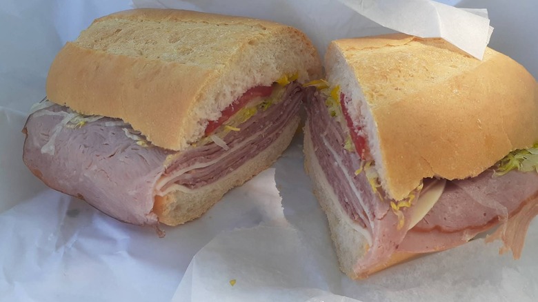 A halved Italian sub on a soft roll, layered with deli meats, cheese, lettuce, tomato, and onions