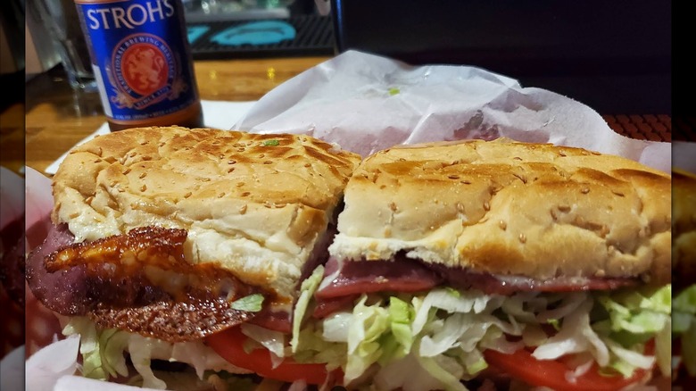 A toasted Italian sub on a sesame-seeded roll filled with deli meats, cheese, lettuce, and tomato