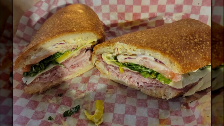 An Italian sub cut in half, showcasing tightly stacked deli meats and cheese with shredded lettuce, and tomato