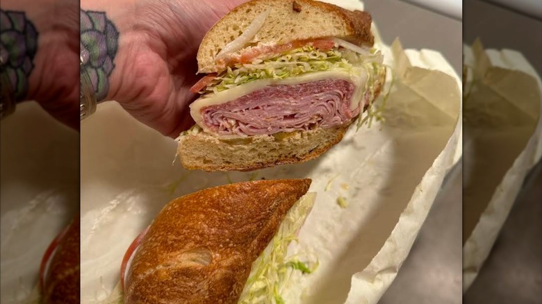 An Italian sub cut in half, showcasing deli meats and cheese with shredded lettuce, and tomato
