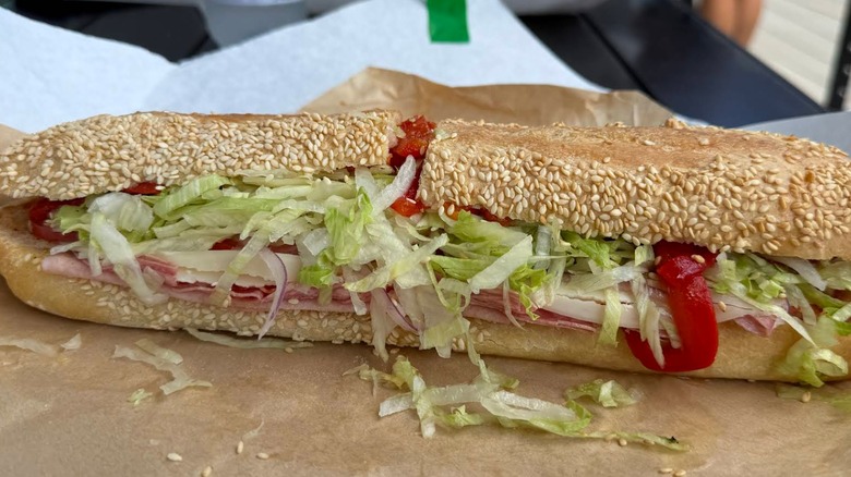 A long sesame-seeded Italian sub filled with deli meats, provolone, shredded lettuce, and bright red roasted peppers
