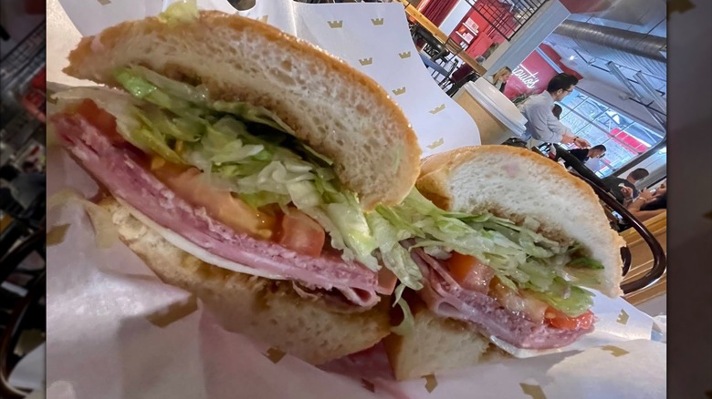An Italian sub cut in half on deli paper, packed with deli meats, lettuce, and tomato with a light drizzle of dressing