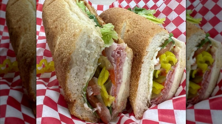 A crusty Italian sub cut in half, packed with deli meats and cheese, lettuce, tomato, and bright yellow banana peppers