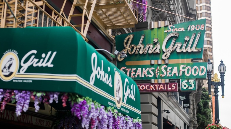 The front entrance of John's Grill featuring the sign and awning with flowers