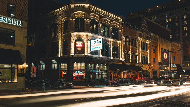 The outside of St. Elmo Steak House at night with cars driving past