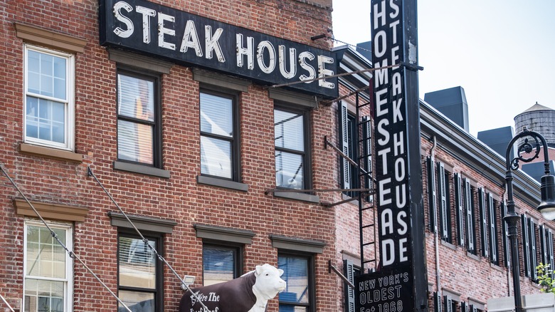 The outside of The Old Homestead Steakhouse with a sign and cow