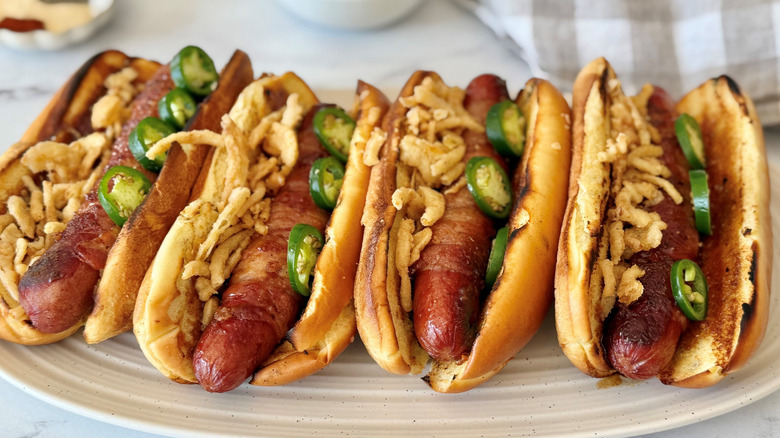 Bacon-wrapped hot dogs topped with jalapeños and crispy onions