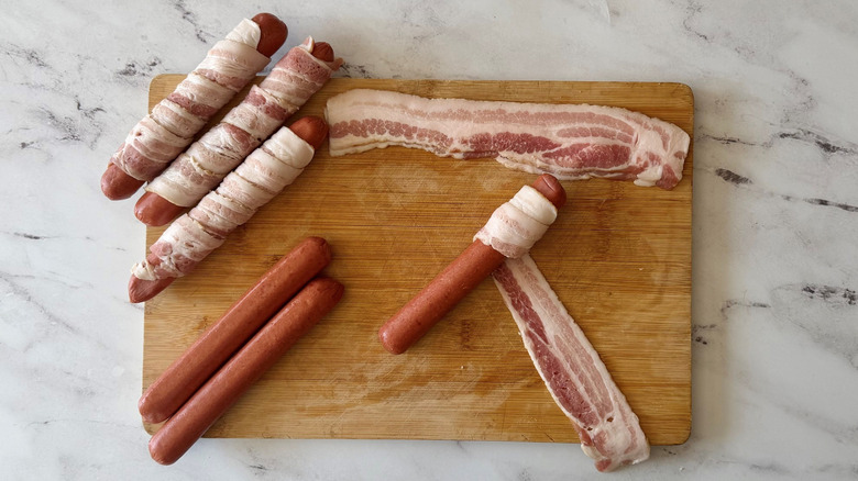 Bacon wrapped hot dogs and plain hot dogs on wooden board