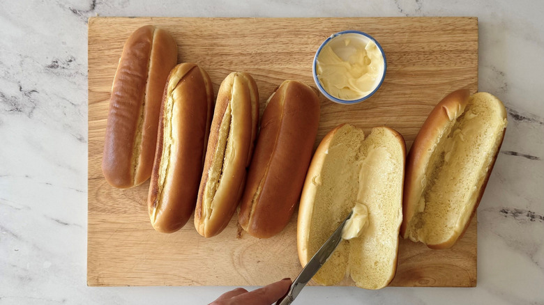 Buttering hot dog buns on wooden board