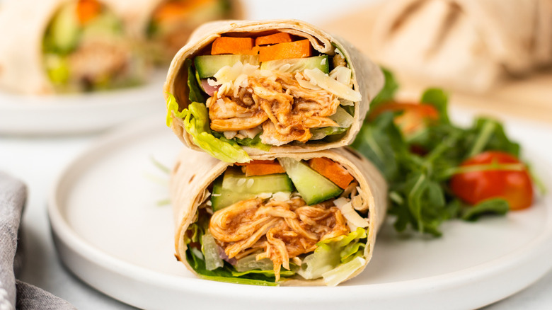 Halved and stacked BBQ chicken and crunchy veggie wrap on plate