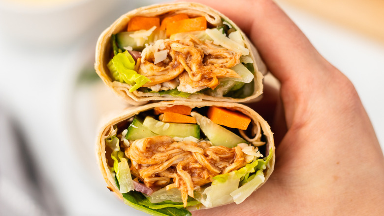 Hand holding halved BBQ chicken and crunchy veggie wrap