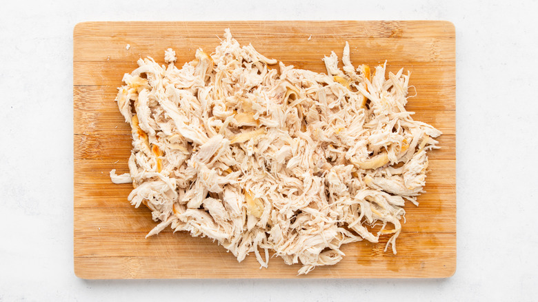 Shredded cooked chicken on wooden cutting board