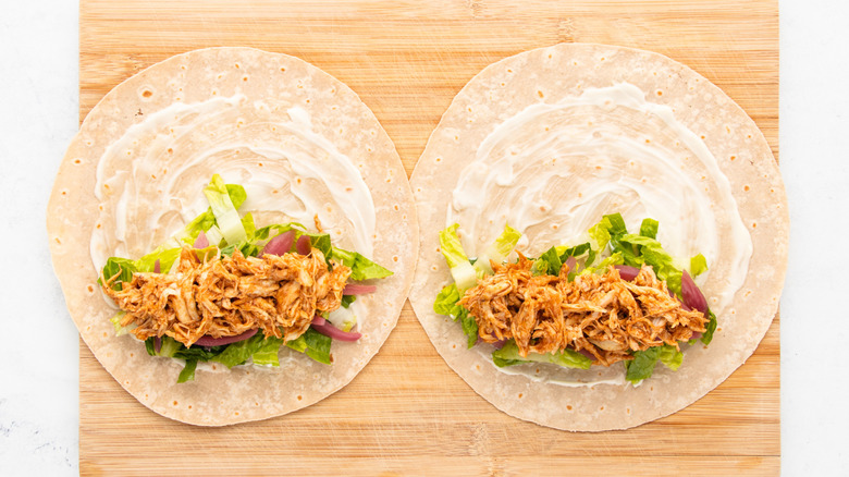 Two flour tortillas topped with mayo, salad, and BBQ chicken