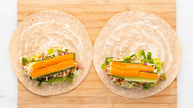 Two flour tortillas topped with mayo, salad, BBQ chicken, and shredded cheese