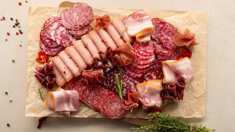 An array of deli meats spread on parchment paper with fresh herbs