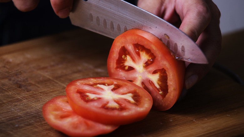 A close-up shot of a person slicing a tomato with a knife