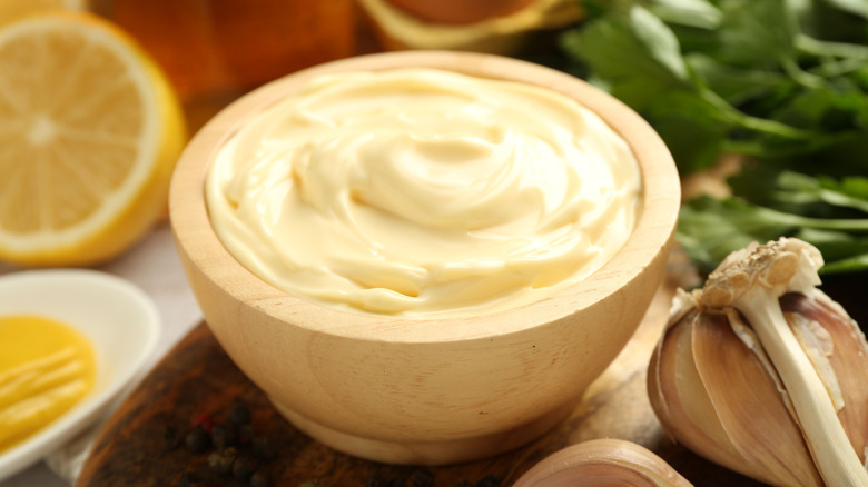 A bowl of mayonnaise next to sliced lemon, garlic, and herbs