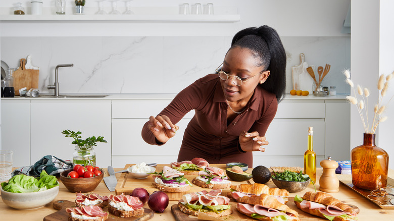 A woman preparing sandwiches with a bunch of ingredients spread out on the table
