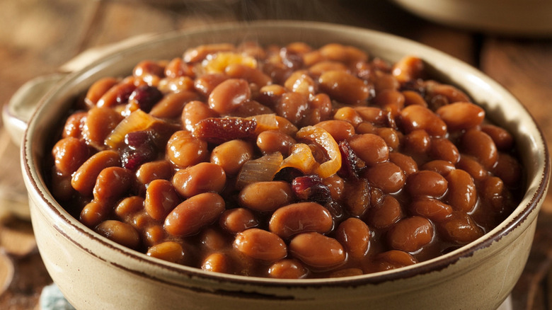 Bowl of saucy baked beans with onions and meat.