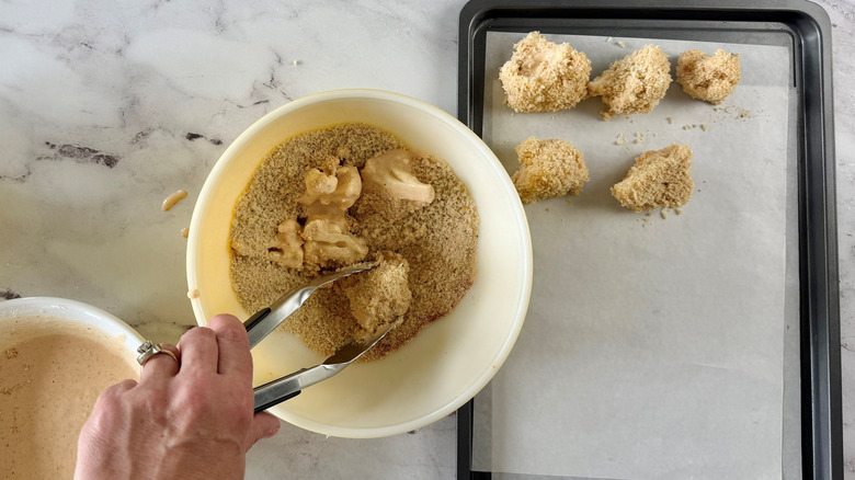 Tongs grabbing cauliflower wing from breadcrumb mixture