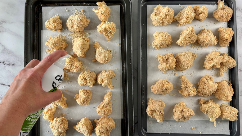 Hand spraying cauliflower wings on baking sheet with cooking spray