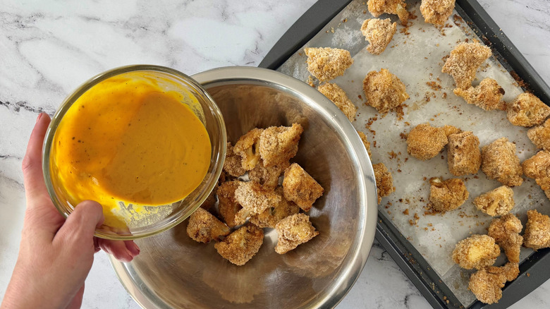 Hand pouring BBQ sauce over cauliflower wings in bowl