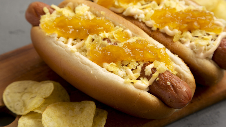 Two Colombian hot dogs served with potato chips on a wooden board.