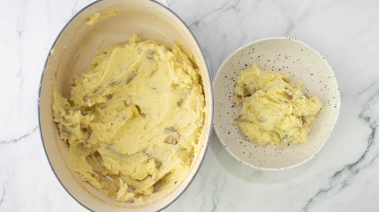 Mashed potatoes in cookware and bowl on marble surface