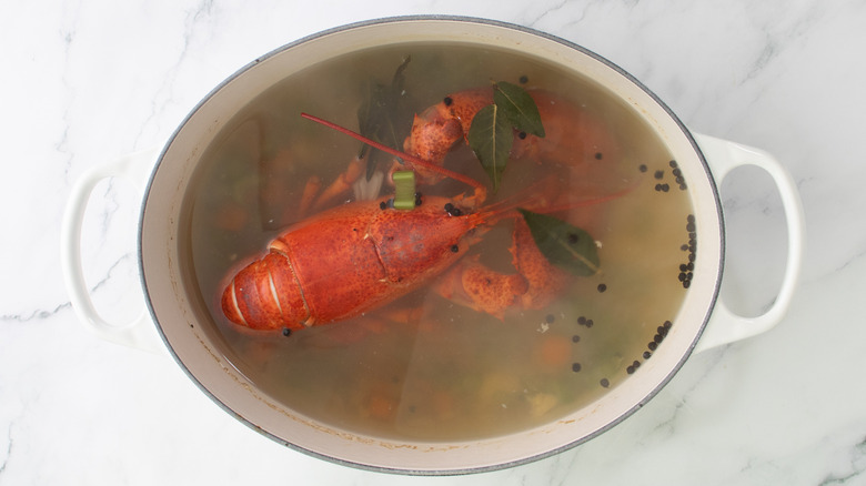 whole lobster cooking in pot of broth with veggies and peppercorns