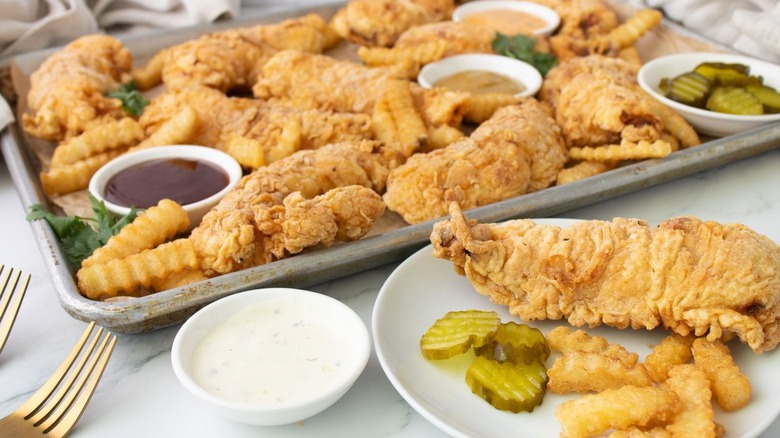 baking sheet covered with crispy chicken tenders, fries, and dips