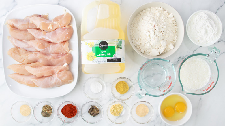Raw chicken tenders laid out on plate and breading ingredients in bowls and measuring cups
