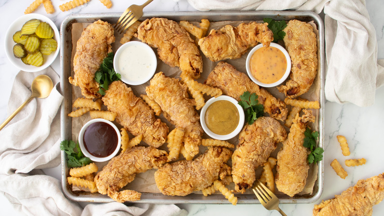 baking sheet with fried chicken tenders, fries, and dips